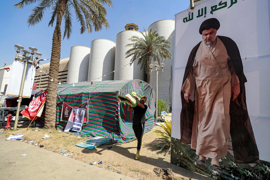 Apoiador do clérigo xiita Moqtada al-Sadr desmonta acampamento na Zona Verde, ao lado de um cartaz do líder religioso