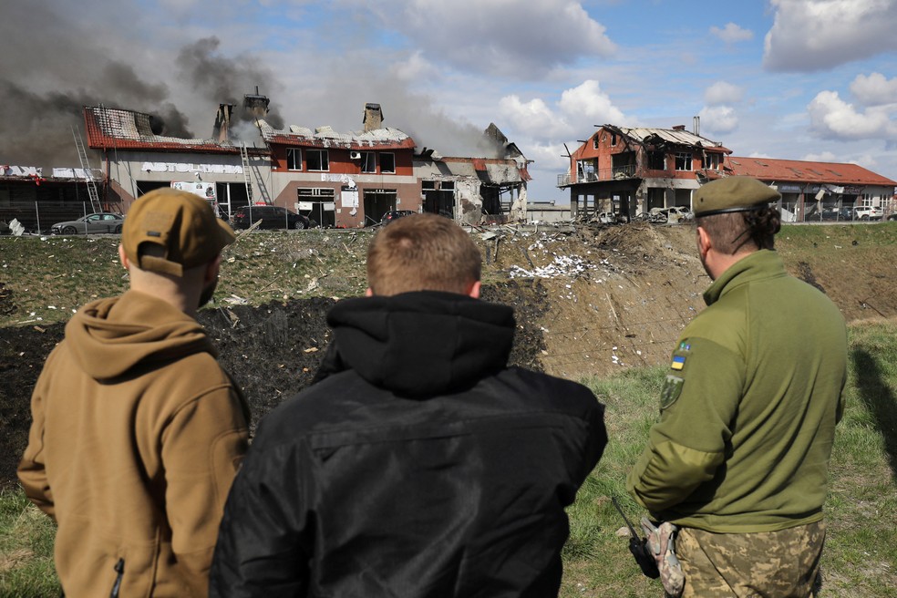 Homens observam instalações e pontos comerciais em Lviv atingidos por bombardeios nesta segunda-feira (18) — Foto: Reuters