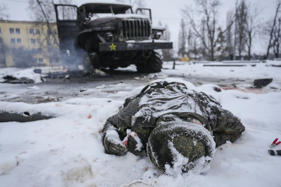 25/02 - O corpo de um soldado é visto coberto de neve ao lado de um veículo lançador de foguetes militares russos destruídos nos arredores de Kharkiv, na Ucrânia, nesta sexta-feira (25) — Foto: Vadim Ghirda/AP