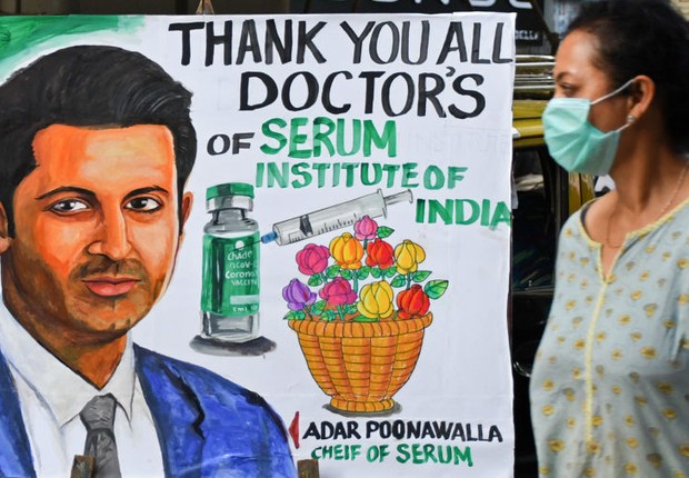 Uma mulher passa por uma pintura dando as boas-vindas ao programa de vacinação da Covid-19 com um retrato de Adar Poonawalla, CEO do Serum Institute of India (Foto: Foto de Ashish Vaishnav / SOPA Images / LightRocket via Getty Images)