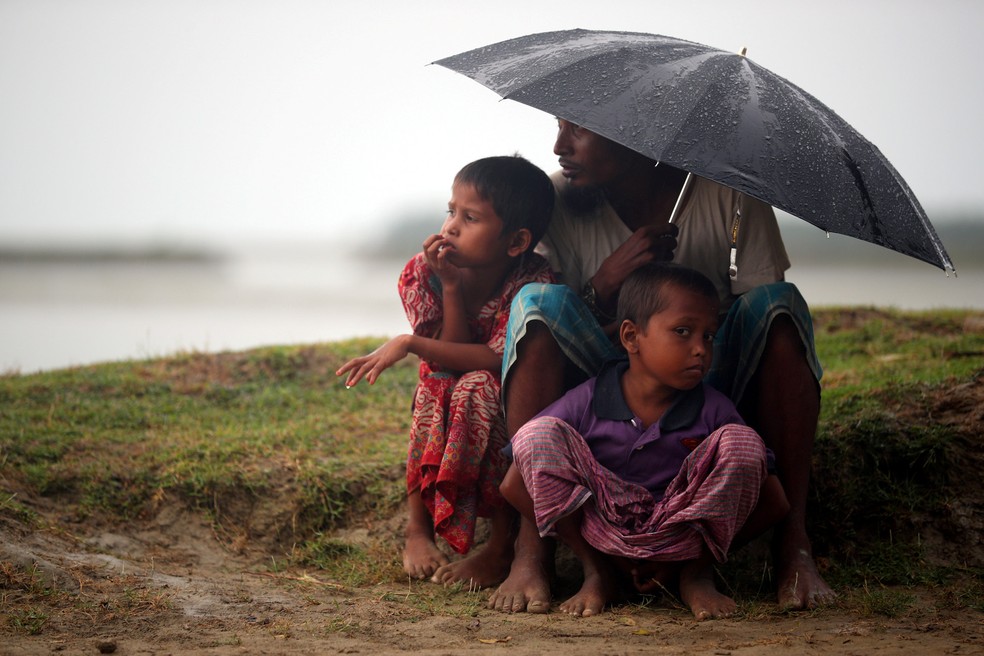 Refugiados rohingya se protegem da chuva enquanto aguardam permissão do exército de Bangladesh para cruzar a fronteira de Mianmar para o país no porto de Teknaf (Foto: Hannah McKay/Reuters)