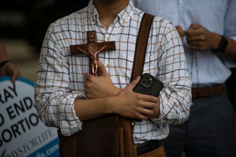 Ativista antiaborto segura crucifixo em frente a manifestantesdo lado de fora da prefeitura em Houston, Texas — Foto: BBC