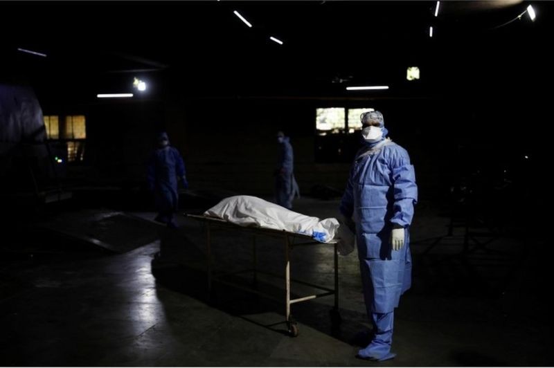 Espera para cremação em Delhi: profissional de saúde ao lado do corpo de um homem que morreu de covid-19 (Foto: Reuters via BBC)