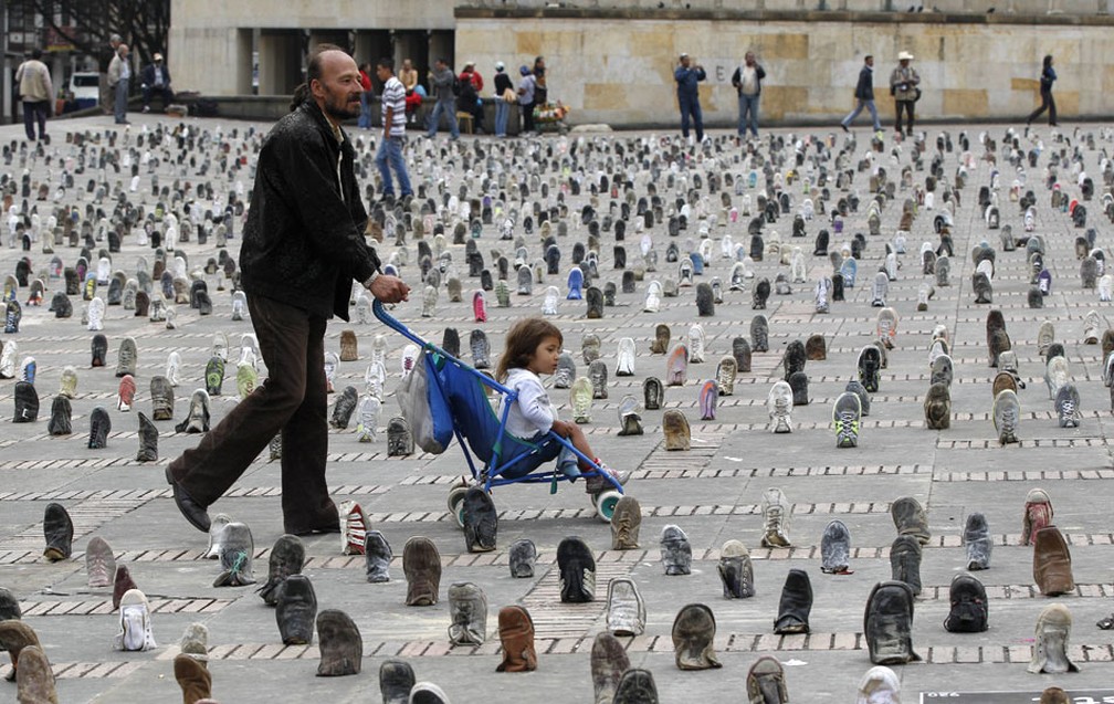 Homem passeia com a filha em meio a instalação de calçados feita em Bogotá, na Colômbia, em obra que marca o Dia Internacional de Alerta sobre Minas Terrestres (Foto: Fernando Vergara/AP)