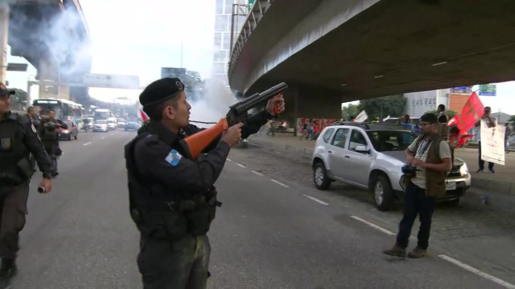 Rio de Janeiro, 7h37: PM saca arma não letal na frente de uma bomba de efeito moral contra manifestantes — Foto: Reprodução/TV Globo