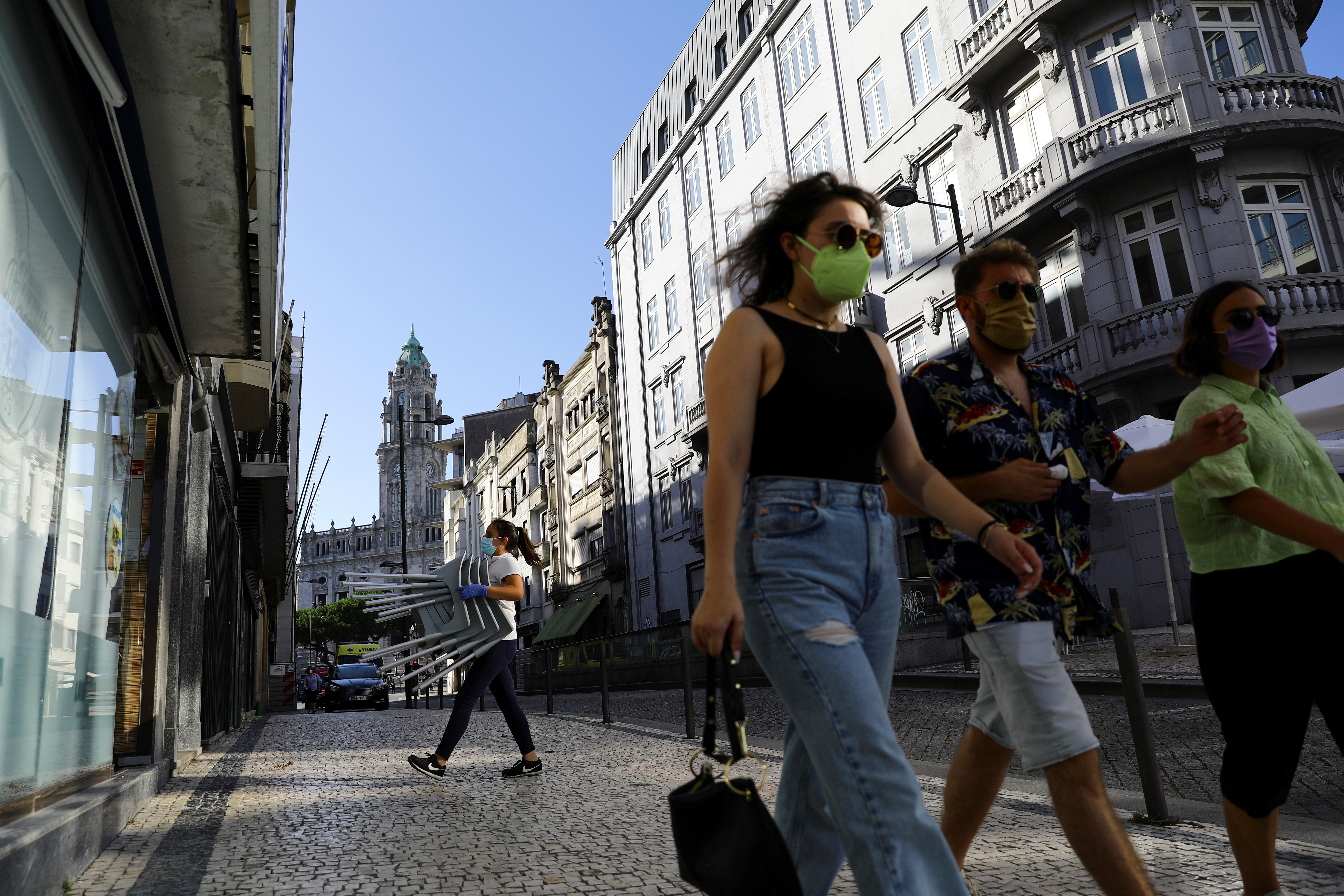 Funcionária transporta cadeiras e pedestres caminham em calçada do Porto