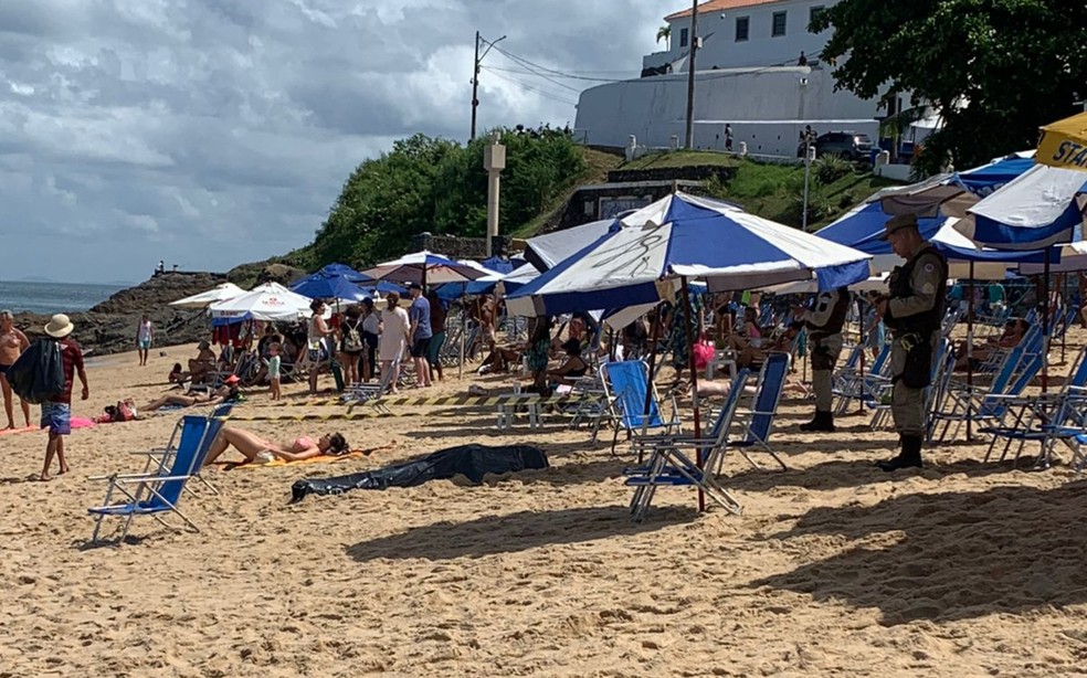 Mulher toma banho de sol próxima do corpo encoberto na praia do Porto da Barra — Foto: Reprodução/Redes Sociais