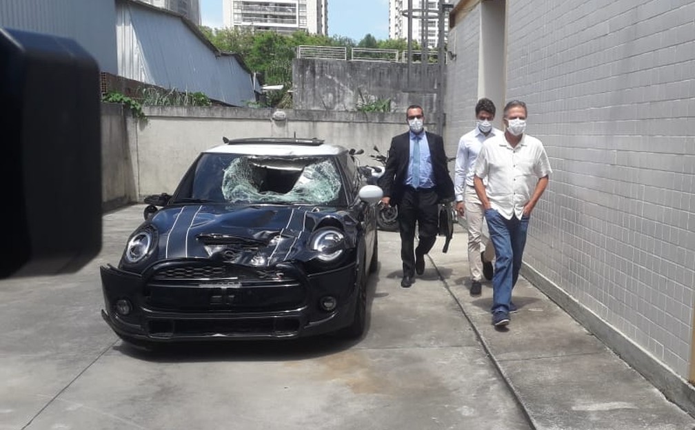 Após prestar depoimento, Marcinho e o pai Sergio Lemos de Oliveira saem da delegacia ao lado do carro do acidente — Foto: Davi Barros / ge