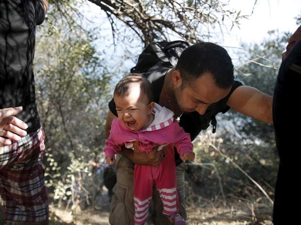 Homem com bebê nos braços escala montanha na ilha de  Lesbos, ao chegar na Grécia neste sábado (22) (Foto: REUTERS/Alkis Konstantinidis)
