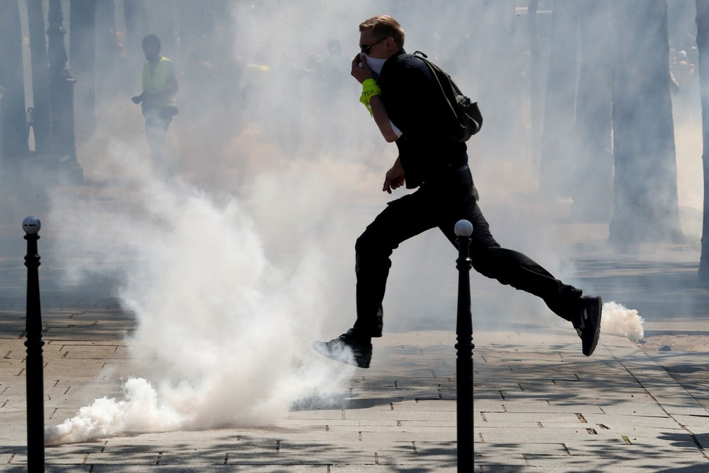 Manifestante cobre rosto enquanto passa por fumaça de gás lacrimogênio durante o 23º dia de protestos dos coletes amarelos — Foto: Yves Herman/Reuters