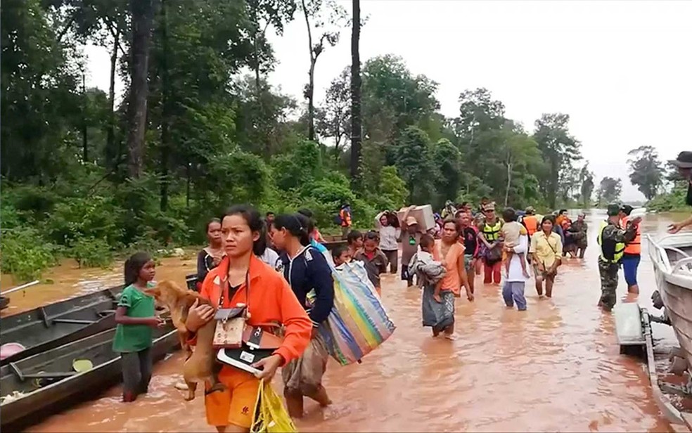 Pessoas caminham por área alagada no Laos (Foto: Attapeu Today / via Reuters)