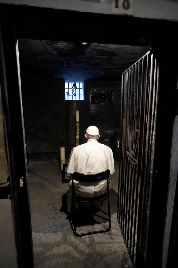 O Papa Francisco reza em uma cela do campo de extermínio nazista de Auschwitz, com a frase 'Arbeit Macht Frei' ('O trabalho liberta', em alemão), em Oswiecim, na Polônia, como parte da programação da Jornada Mundial da Juventude (Foto: Reuters/Osservatore Romano)