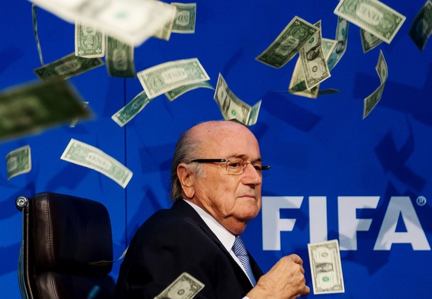 O presidente da Fifa, Joseph Blatter, é alvo de uma ação do comediante Simon Brodkin (que não aparece na foto), que interrompeu uma coletiva de imprensa da entidade para atirar dólares em Blatter, em alusão à corrupção na Fifa (Foto: Philipp Schmidli/Getty Images)
