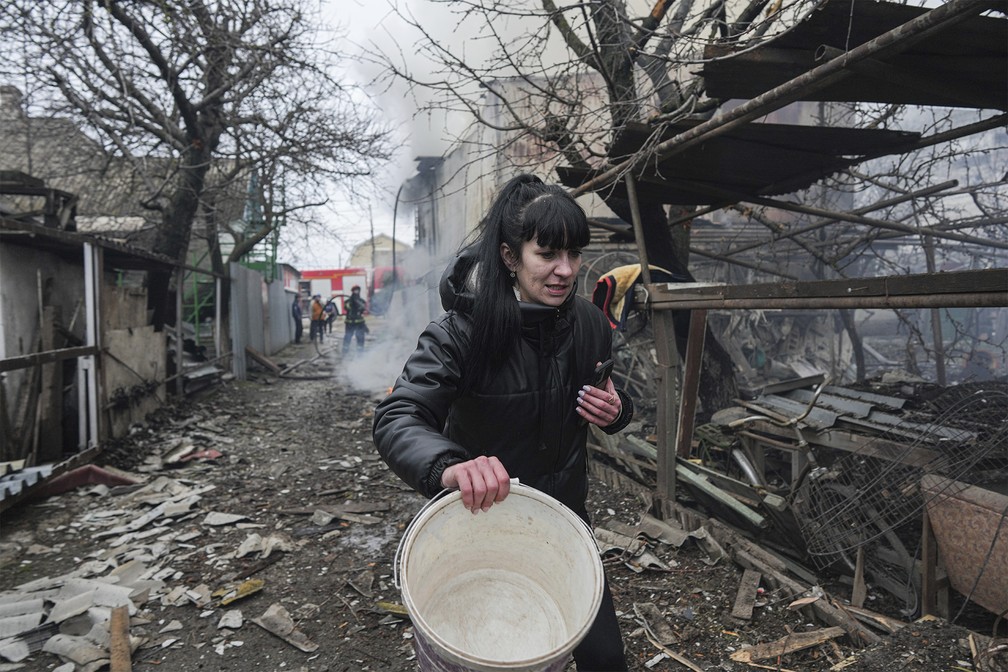 Uma mulher passa pelos escombros após o bombardeio russo, em Mariupol, Ucrânia, nesta quinta-feira (24) — Foto: Evgeniy Maloletka/AP