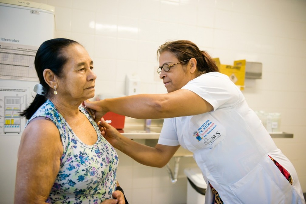 Mulher recebe vacina contra a gripe em VitÃ³ria, no EspÃ­rito Santo, durante a campanha de imunizaÃ§Ã£o em 2018  (Foto: Diego Alves/ Prefeitura de VitÃ³ria)