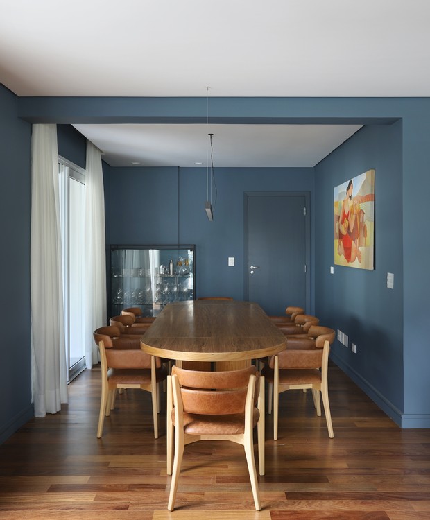 SALA DE JANTAR | A área de jantar recebeu a mesma tinta azul que percorre a entrada do imóvel. Mesa desenhada pelo escritório, cristaleira da Dunelli e cortinas da Casa 4 (Foto: Mariana Orsi / Divulgação )