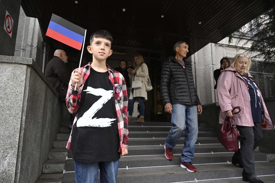 Menino usa blusa com símbolo do Exército russo e carrega bandeira da autoproclamada república de Donetsk em frente à embaixada da região em Moscou