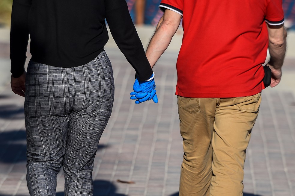 Um casal usando luvas é visto de mãos dadas em South Beach, Miami — Foto: Chandan Khanna/AFP