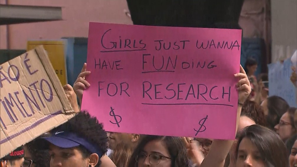 Cartaz diz, em inglÃªs, que "garotas sÃ³ querem fundos para pesquisa", durante protesto em Belo Horizonte â Foto: ReproduÃ§Ã£o/TV Globo