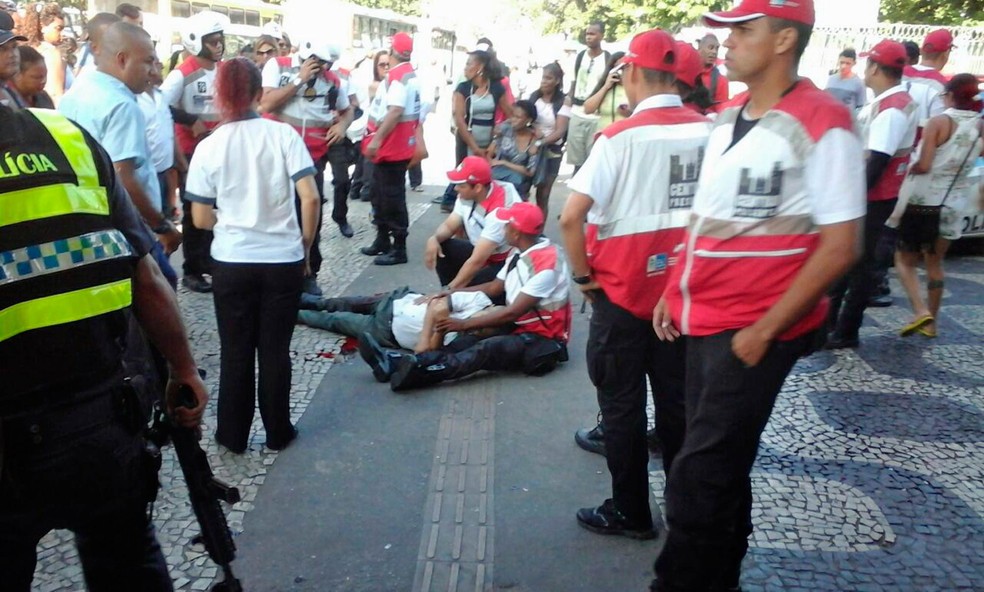 Um dos baleados durante o tiroteio é ajudado por agentes da Operação Centro Presente (Foto: Guilherme Pinto/Extra/Agência O Globo)