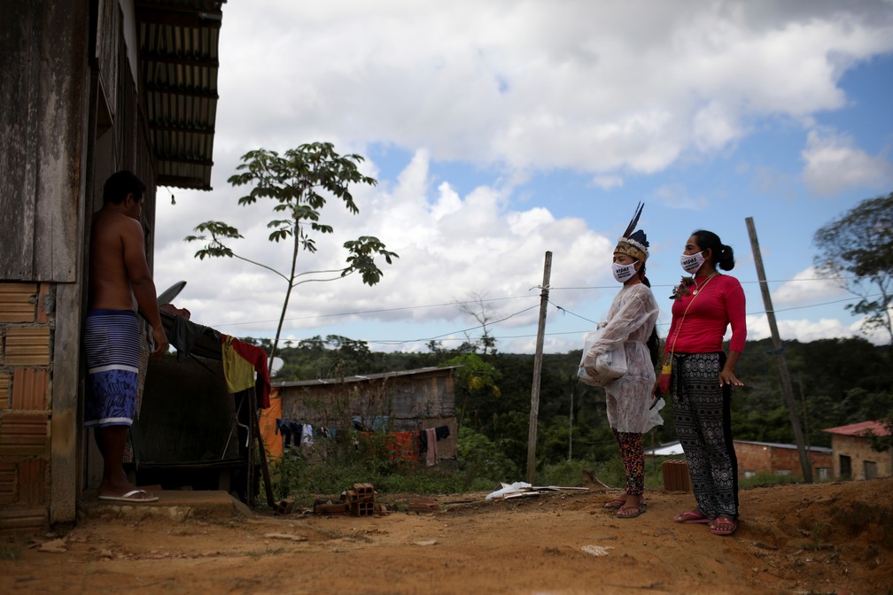 Vanda e a professora e artista Natalina Martins, da tribo Baré,  conversam com um vizinho na entrada de sua casa — Foto: Bruno Kelly/Reuters