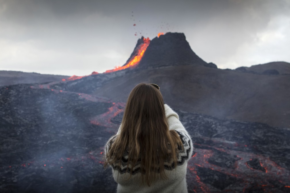 Mulher tira foto de lava jorrando de vulcão em erupção na península de Reykjanes, no sudoeste da Islândia, na terça-feira (23) — Foto: Marco Di Marco/AP