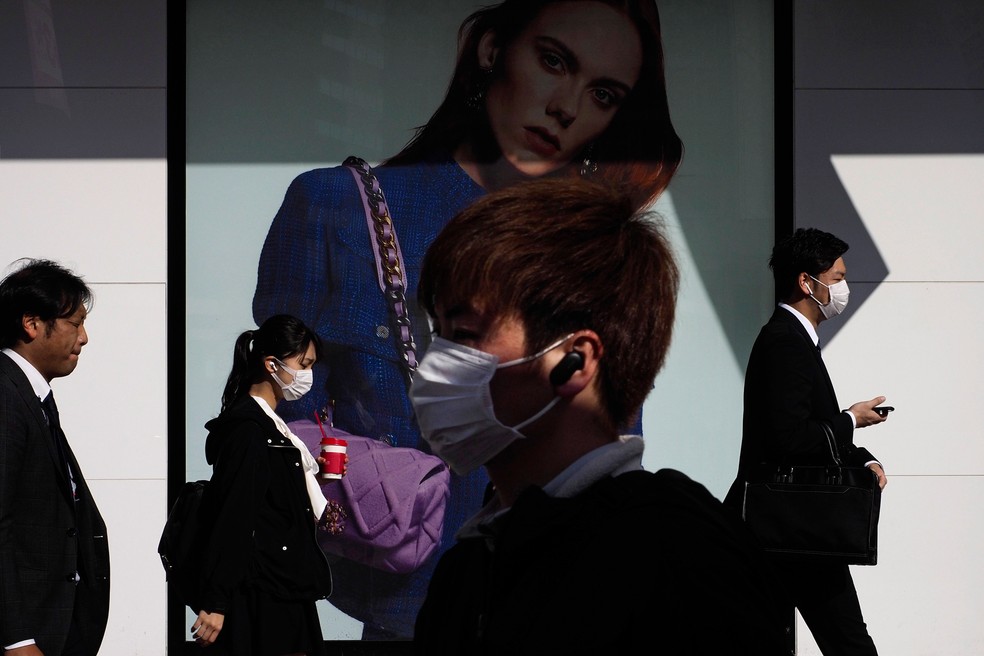 Passageiros passam por um anúncio fora da estação Shinjuku, em Tóquio, nesta quinta-feira (26)  — Foto: Jae C. Hong/AP 