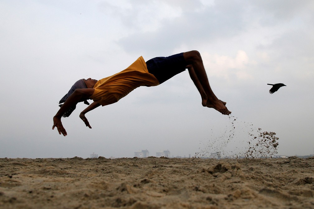 11 de março - Um menino pratica cambalhotas enquanto faz exercícios em uma praia de Kochi, na Índia — Foto: Sivaram V/Reuters