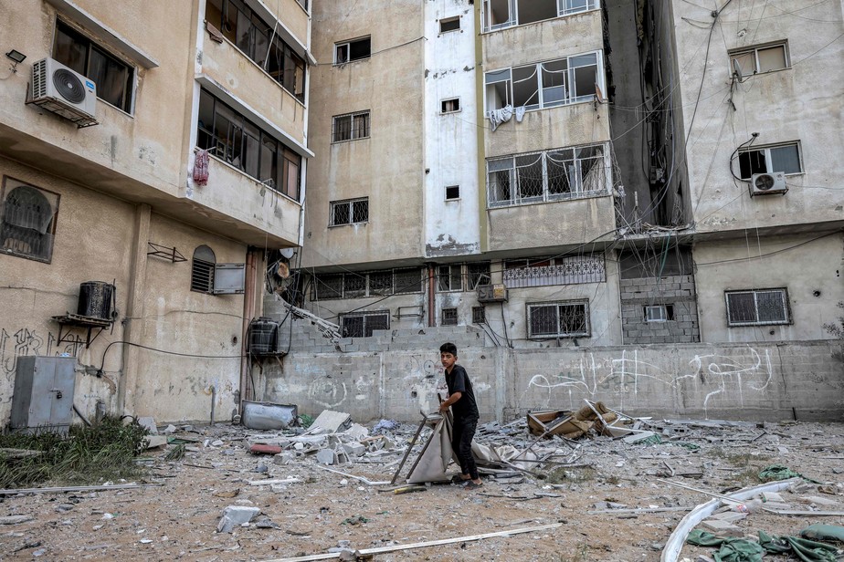 Garoto caminha entre escombros de prédio atingido por foguetes israelenses em Gaza