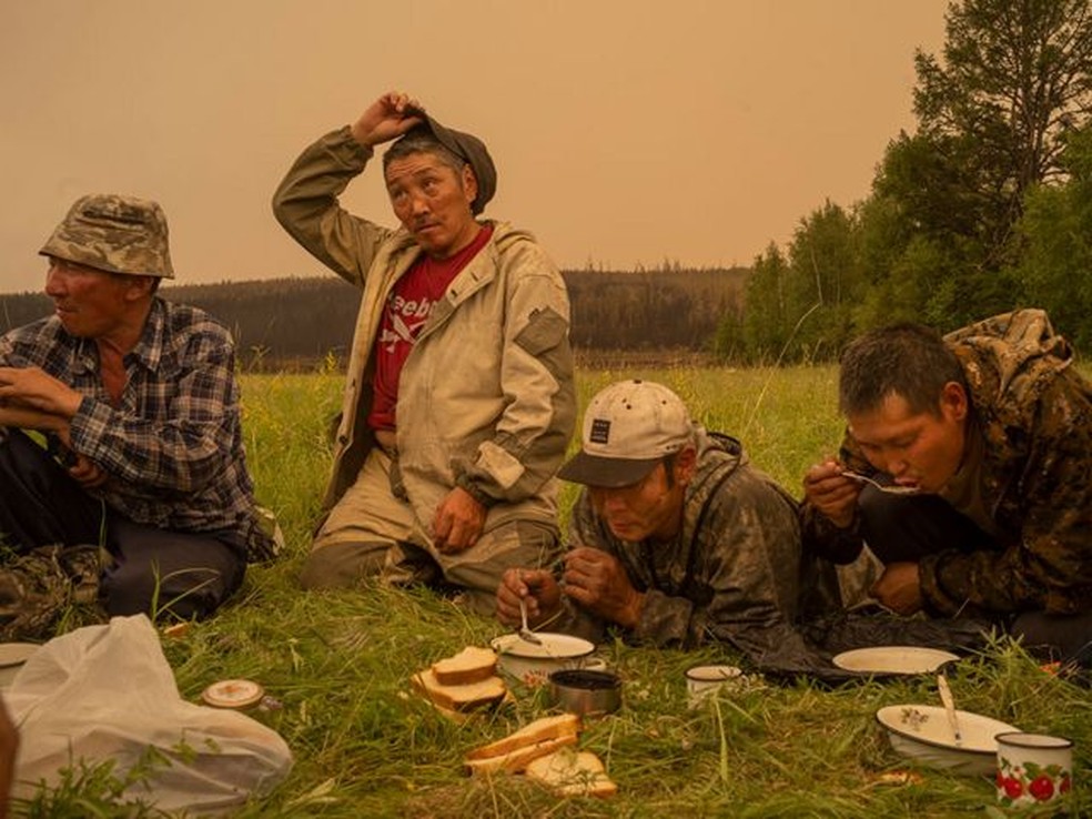 Voluntários locais de combate a incêndios fazem uma pausa para comer em um campo em Magaras, Sakha central, Sibéria, Rússia, em 1º de julho de 2021 — Foto: Nanna Heitmann para Magnum Photos