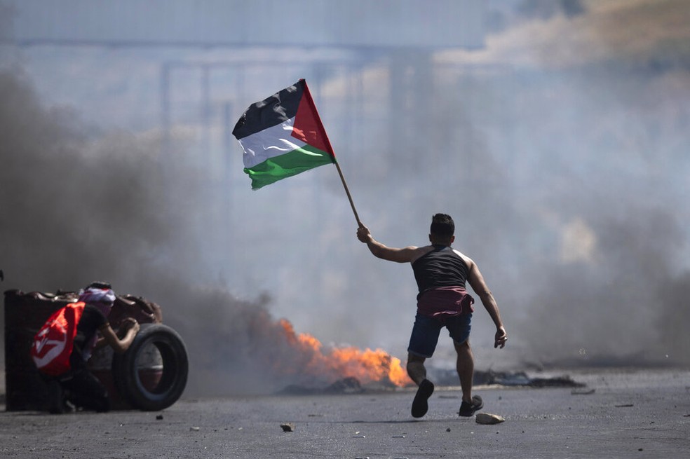 Manifestante levanta bandeira da Palestina durante protesto em Nablus, na Cisjordânia, contra ataques israelenses nesta sexta-feira (14) — Foto: Majdi Mohammed/AP Photo
