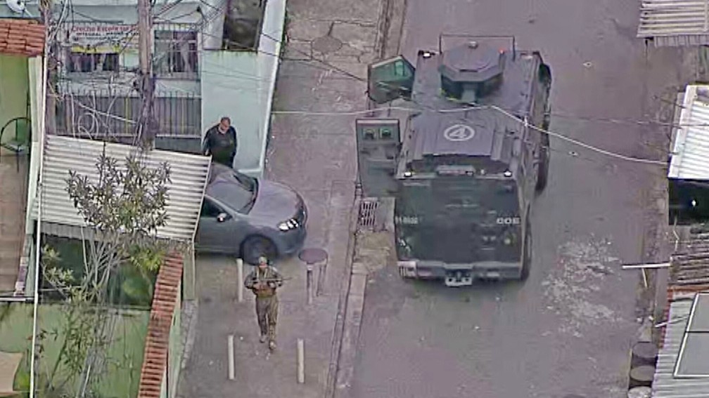 Policial patrulha a Vila Cruzeiro ao lado de um Caveirão — Foto: Reprodução/TV Globo