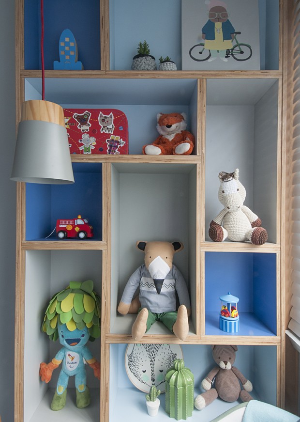 A estante, com apenas 23 cm de profundidade, é revestida em fórmica azul e cinza. Possui diferentes alturas de nichos para organizar os brinquedos, além de trazer dinâmica ao quarto. (Foto: Divulgação/Ana Yoshida)