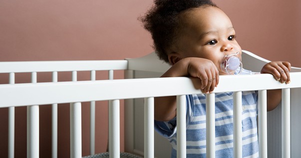 Bebê com chupeta em pé no berço (Foto: Shutterstock)