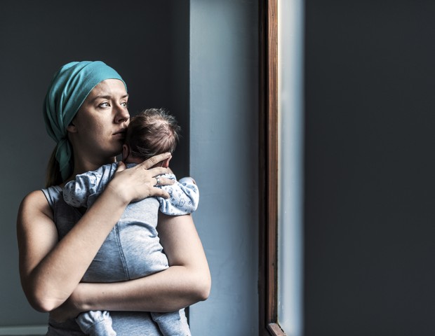 Mãe segurando bebê e olhando pra janela (Foto: Getty Images)