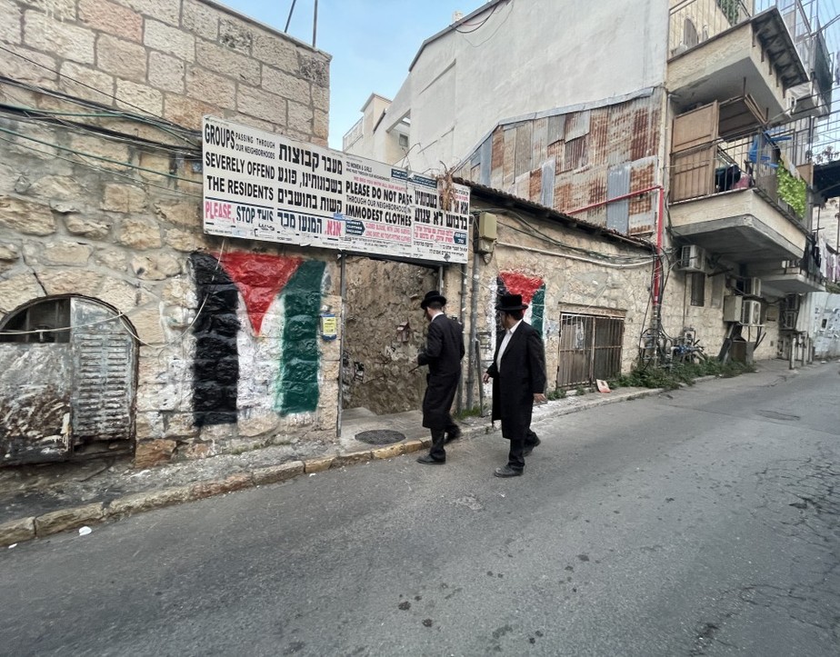 Judeus ultraortodoxos passam por uma bandeira palestina pichada em um muro em Mea Shearim, Jerusalém: os próprios moradores pintam símbolos para espantar pessoas de fora que queiram comprar imóveis no bairro