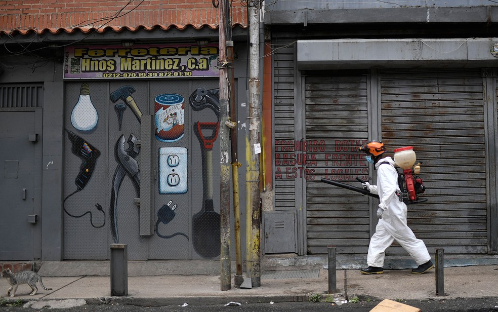 Funcionário municipal espalha desinfetante em fachadas de lojas em Caracas, na Venezuela, em foto de 8 de agosto — Foto: AP Photo/Matias Delacroix
