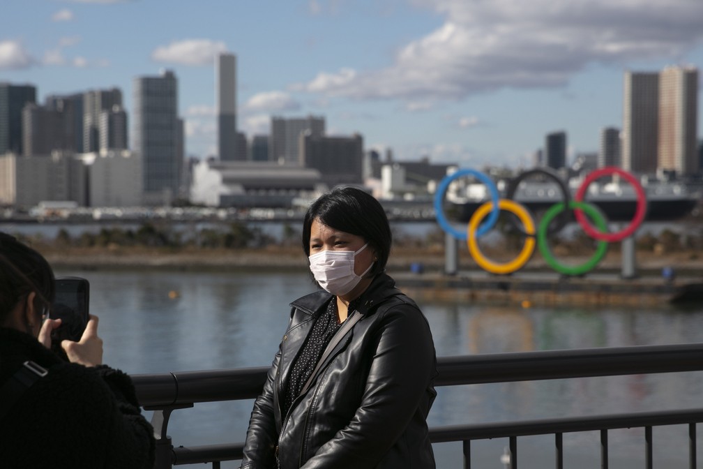 Turista com máscara posa para foto em frente aos anéis olímpicos na Baía de Tóquio, no Japão — Foto: Jae C. Hong, File/AP Photo