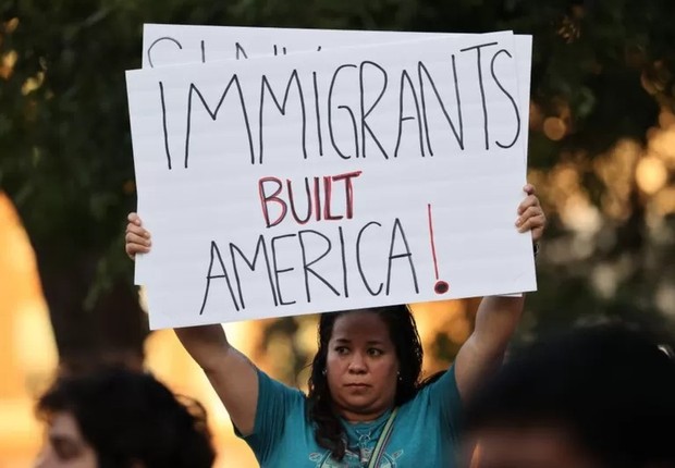 Uma mulher presente na vigília segura um cartaz em que se lê: 'Imigrantes construíram a América' (Foto: GETTY IMAGES via BBC)