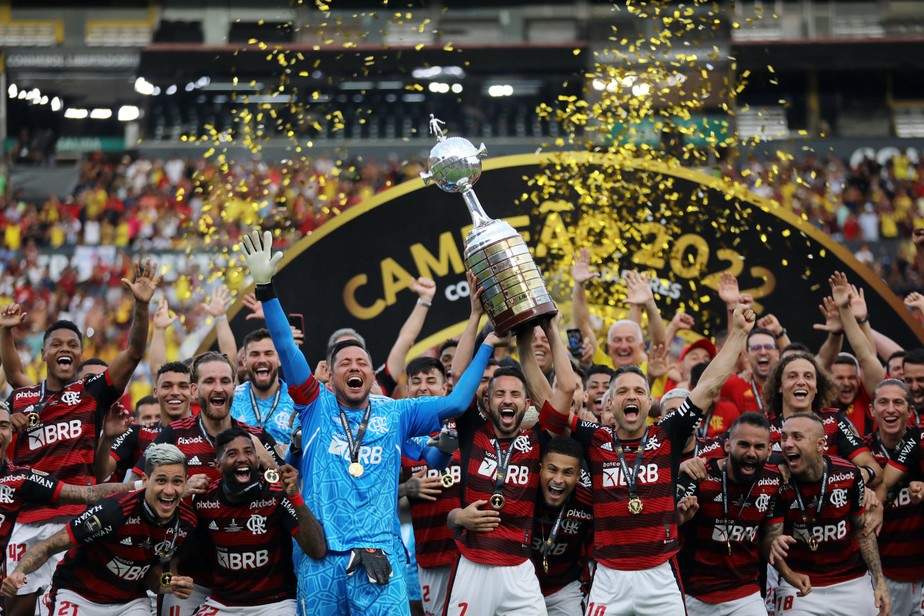 Jogadores do Flamengo comemoram título da Libertadores de 2022. Éverton ribeiro, que carrega o 7 no calção, levanta a taça ao lado do goleiro Diego Alves, de azul, e do meia Diego Ribas. 