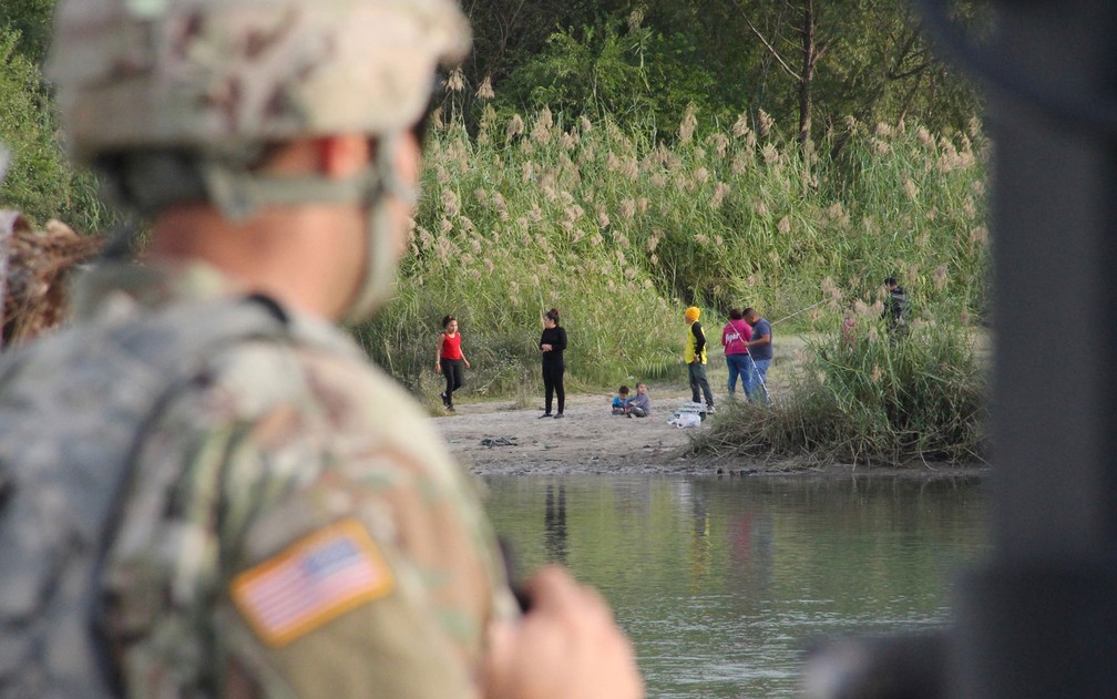 Um soldado do 19º Batalhão de Engenharia de Kentucky, em Laredo, no Texas, observa pessoas em Nuevo Laredo, México, do outro lado do Rio Grande, no domingo (18) — Foto: Thomas Watkins/AFP