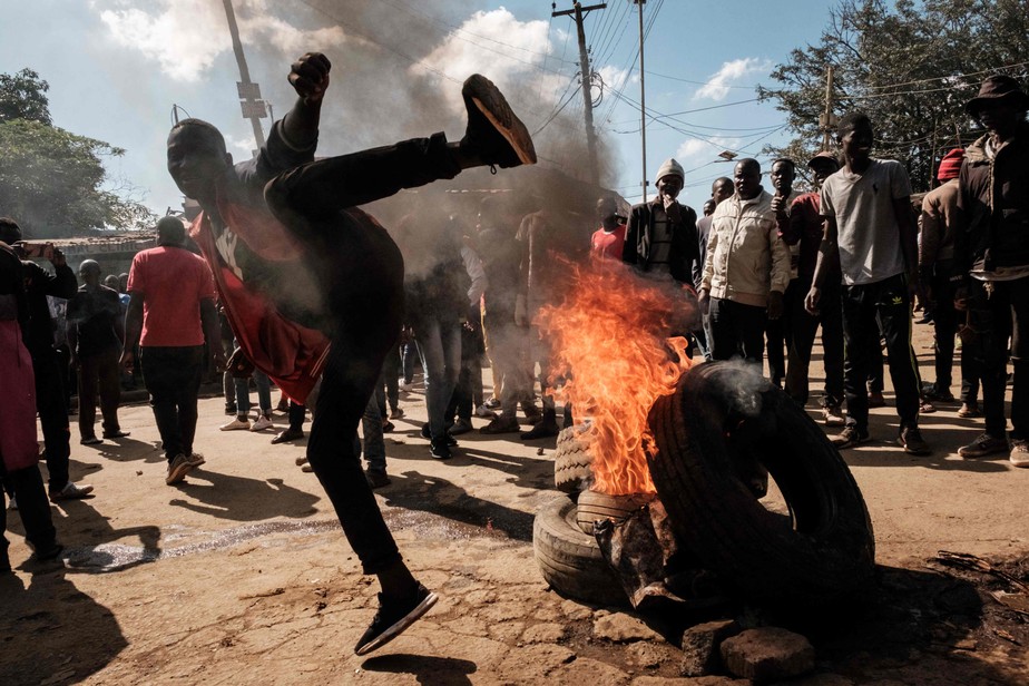 Manifestante gesticula ao lado de uma barricada em chamas durante um protesto contra o governo do Quênia, em Kibera, Nairóbi
