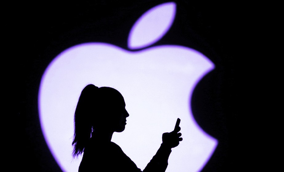 Mulher usa celular diante de logotipo da Apple