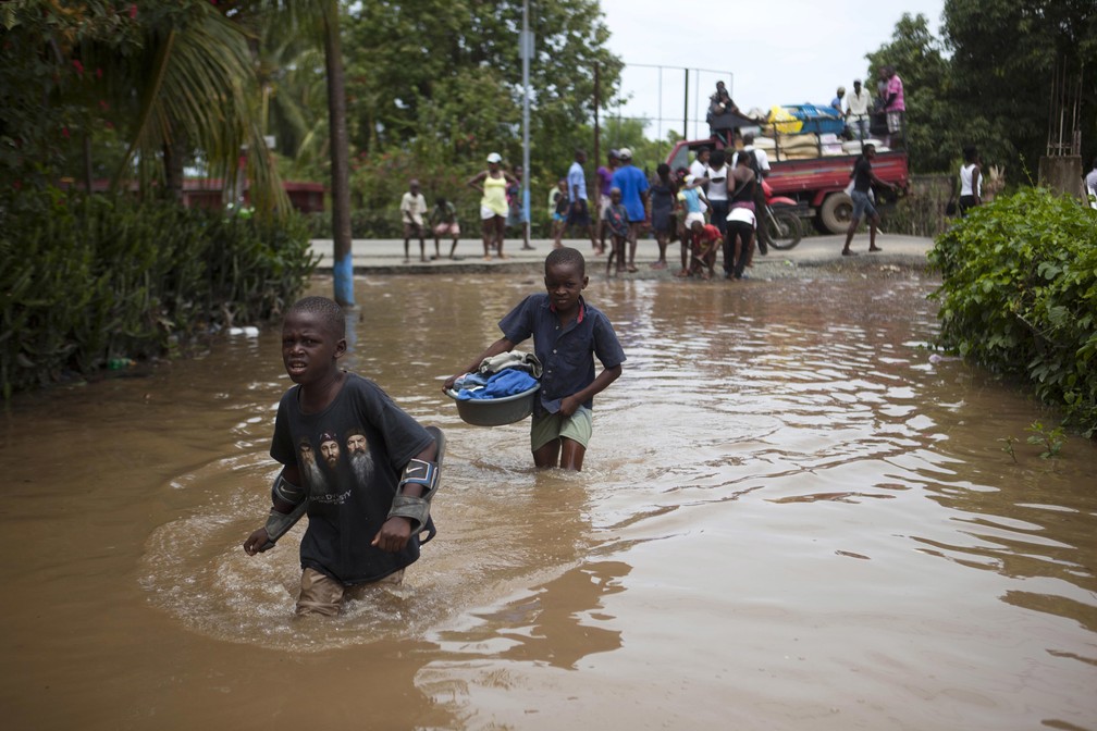 Meninos atravessam as águas das inundações causadas por fortes chuvas provocadas pelo furacão Irma, em Fort-Liberte, no Haiti (Foto: Dieu Nalio Chery/AP)