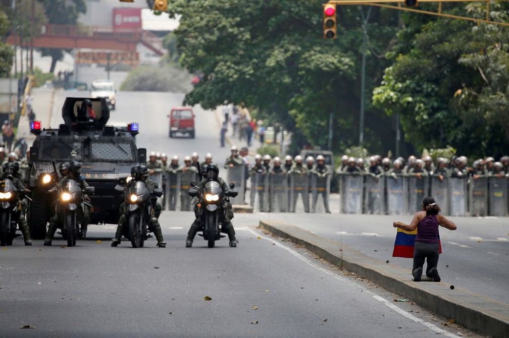 Manifestante com bandeira da Venezuela diante de policiais durante marcha da oposição nesta quinta-feira (20) em Caracas (Foto: REUTERS/Carlos Garcia Rawlins)