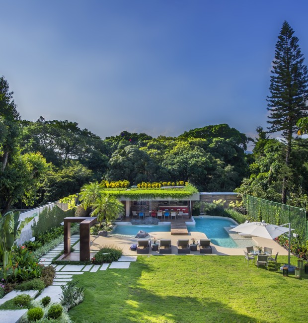 Vista geral do espaço de lazer mostra o gramado, a piscina de formato orgânico e a grande varanda com sua cobertura verde (Foto: Marcio Irala/Divulgação)