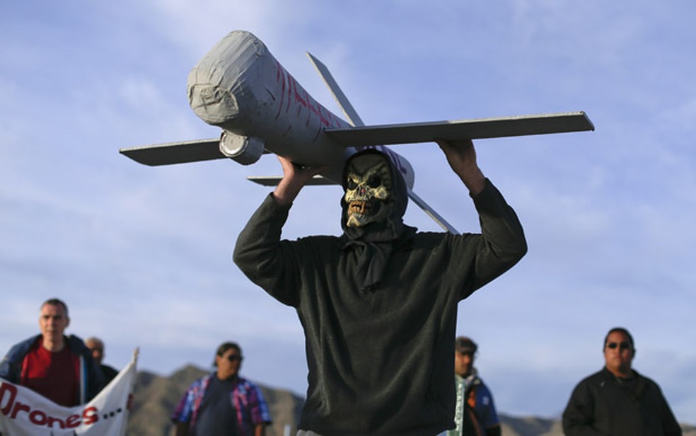 Manifestante mascarado carrega um modelo de drone usado pela Força Aérea nos EUA (Foto: Julie Jacobson/AP)