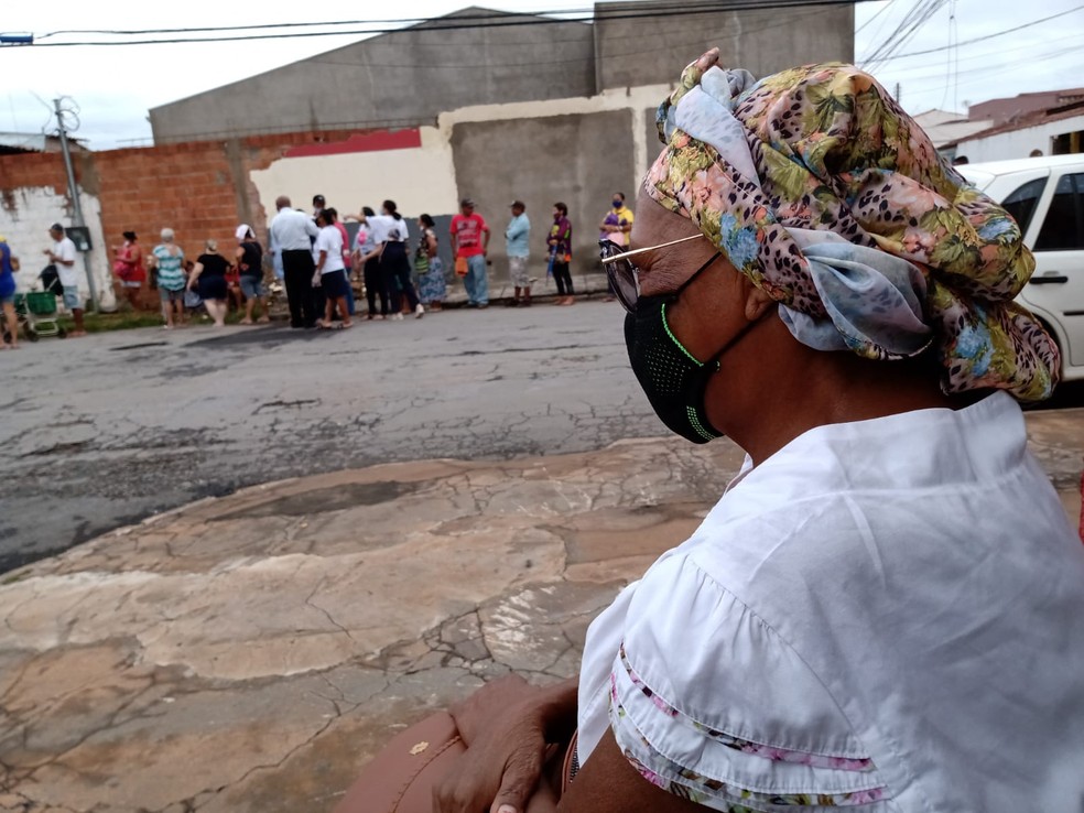 Maria de Lurdes, 65 anos, aguarda na "fila dos ossinhos" sentada do outro lado da rua, em Cuiabá — Foto: Rogério Júnior/g1 MT