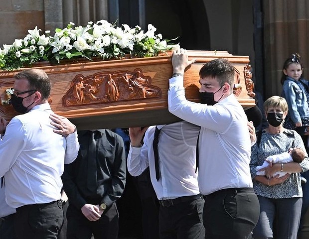 Bebê é carregada atrás do caixão da mãe, que morreu de covid (Foto: Reprodução/Mirror)