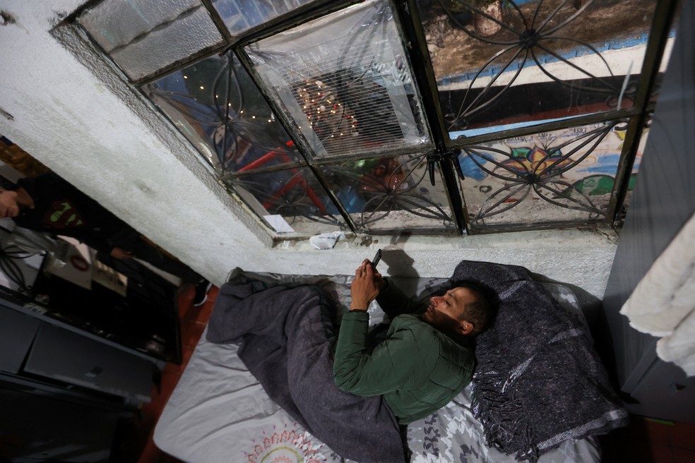 Um migrante da Venezuela usa um telefone coberto com um cobertor, durante as festividades de Natal em um abrigo na Cidade do México — Foto: Reuters